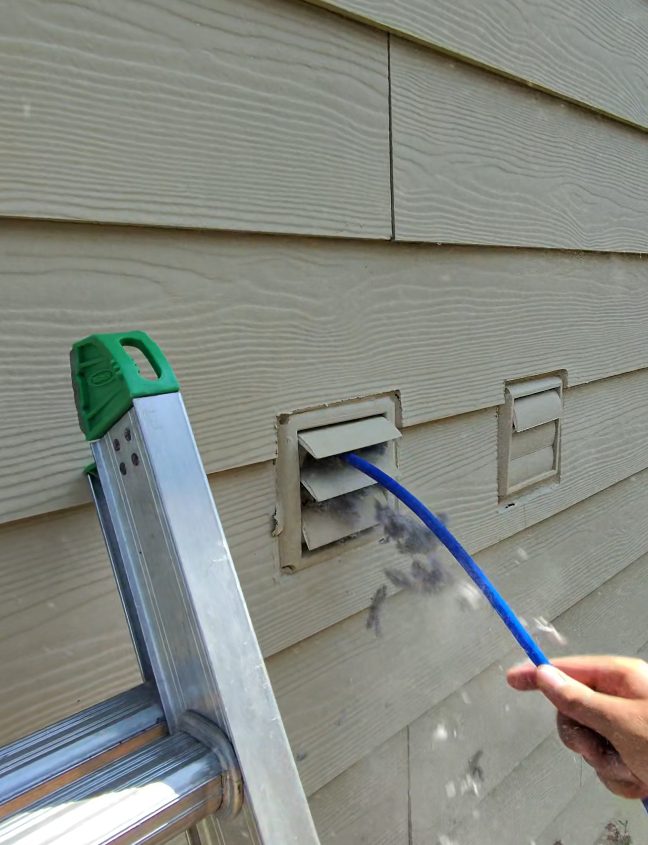 Lint blowing out of a dryer vent while it is cleaned from the outside